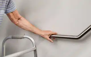 Senior person with a walker holding onto a handrail for support, highlighting safe aging in place.