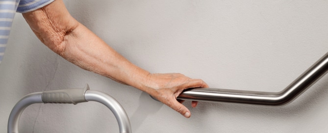 Senior person with a walker holding onto a handrail for support, highlighting safe aging in place.